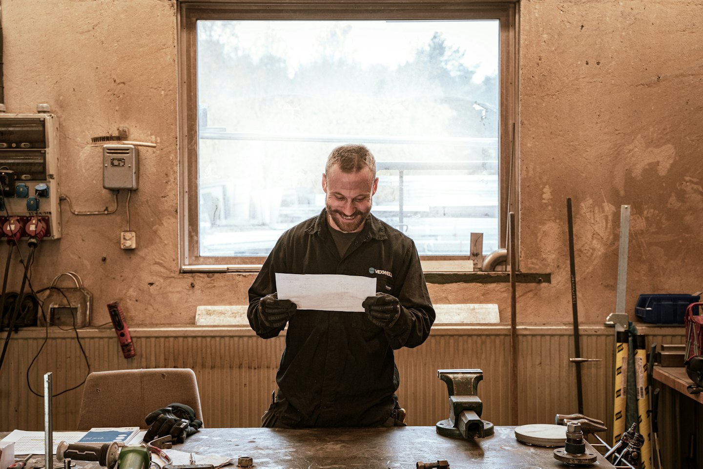 Technician smiles while inspecting paper at a workshop workbench.