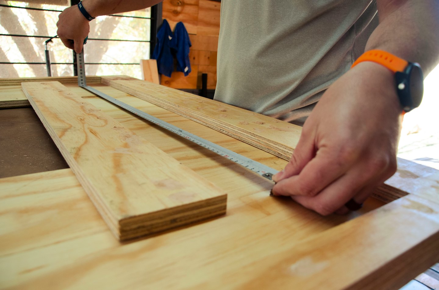 Hands measuring plywood with a tape measure.