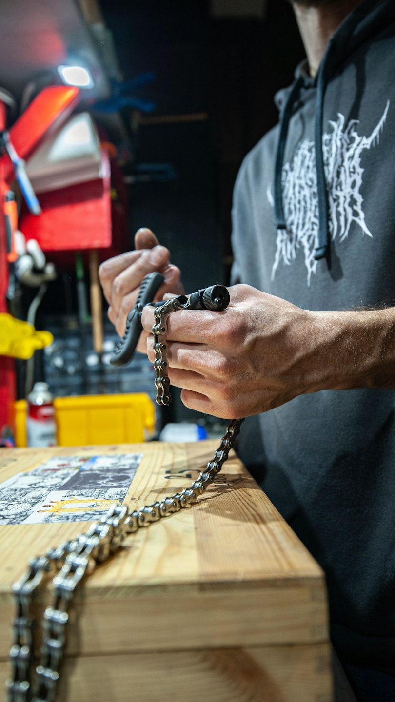 Hands repairing a bicycle chain on a wooden workbench.